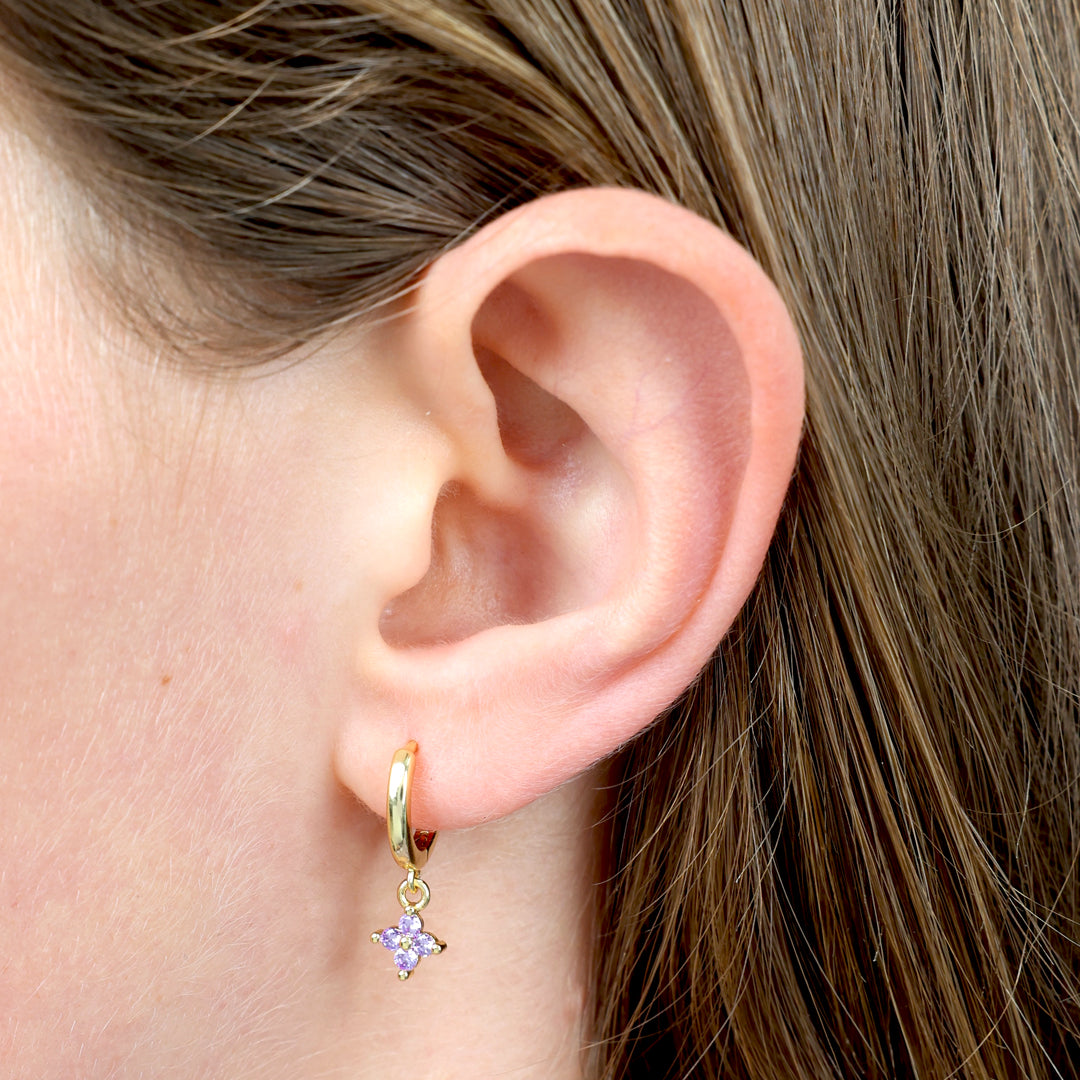 Close-up of an ear wearing a gold earring with a star-shaped purple gem.