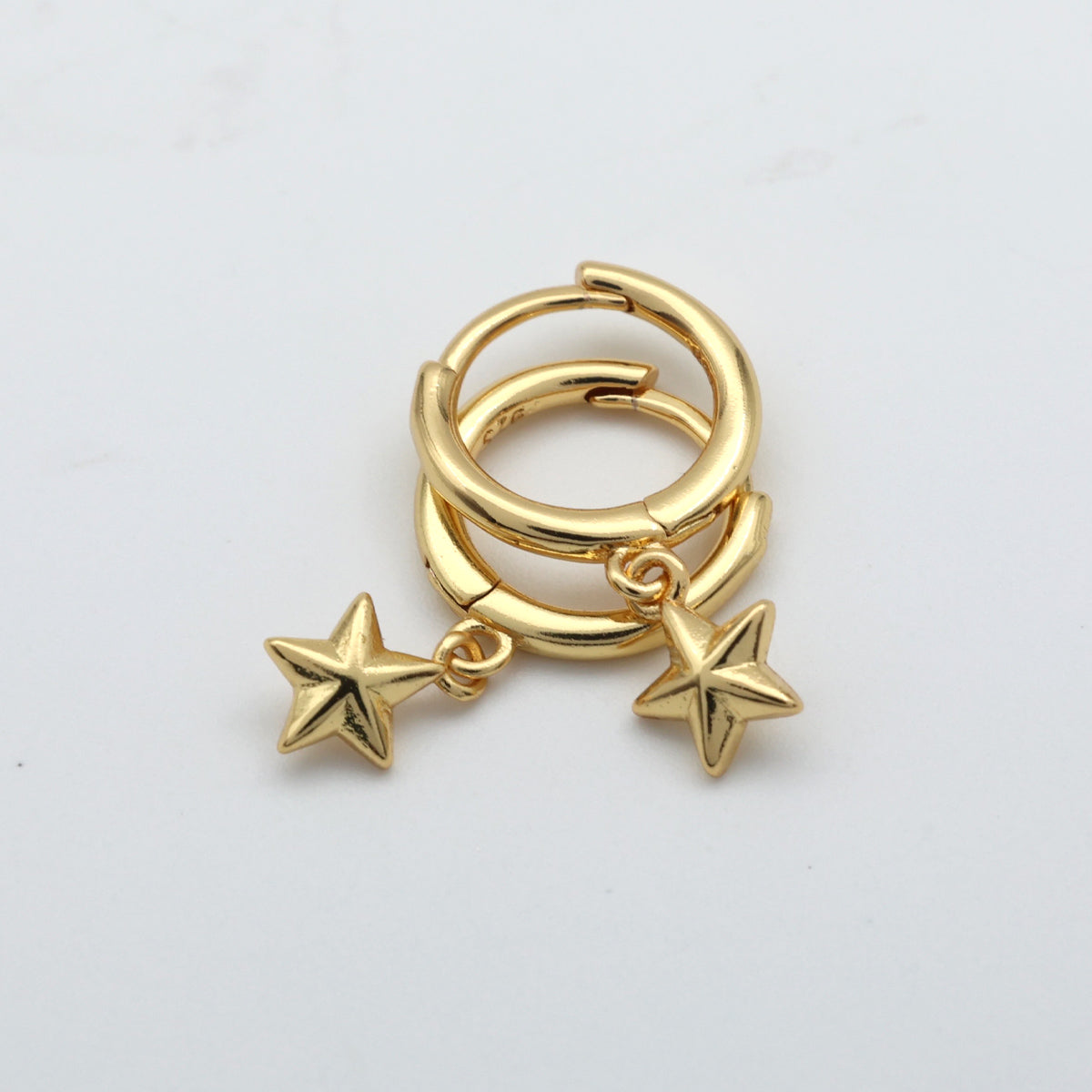 Gold hoop earrings with star charms on a light gray background