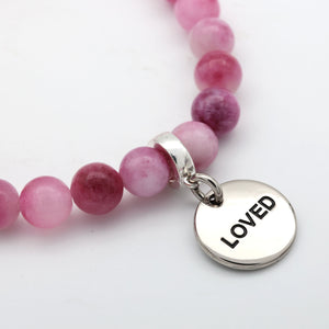 Pink beaded bracelet with a silver charm displaying the word 'LOVED' on a white background