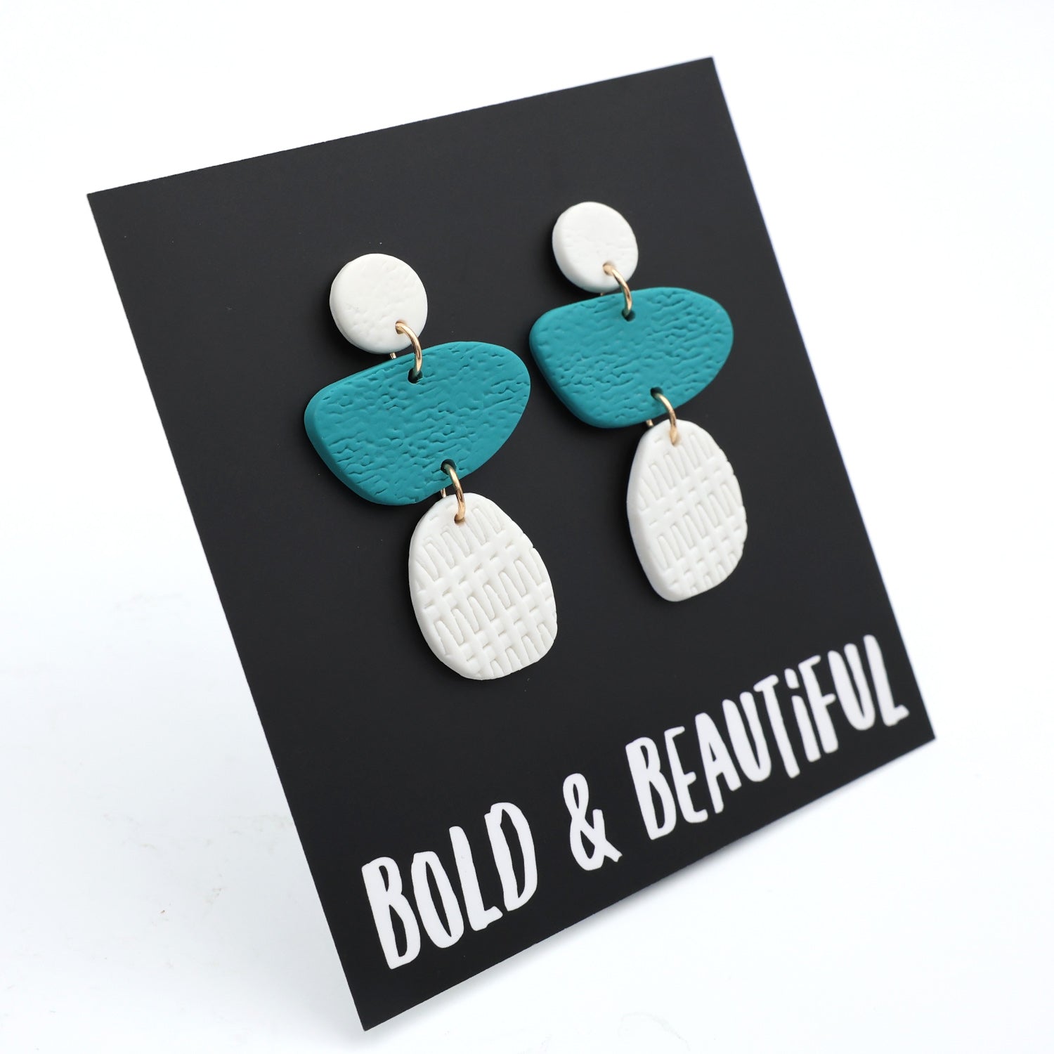 Pair of earrings with blue and white teardrop shapes on a black background with 'Bold & Beautiful' text.