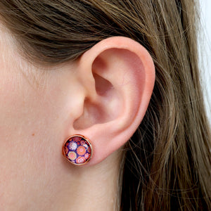 Close-up of an ear wearing a colorful round earring with a blurred background