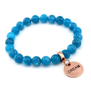 Blue beaded bracelet with a rose gold tag displaying the word 'DREAM' on a white background