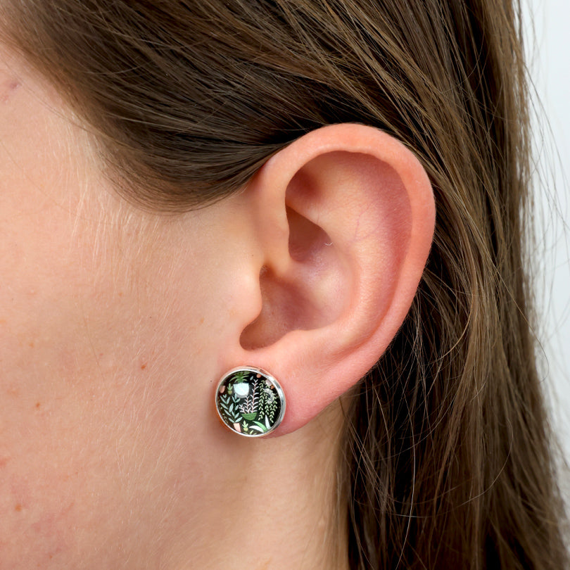 Close-up of an ear wearing a green and gold earring with a white pearl.