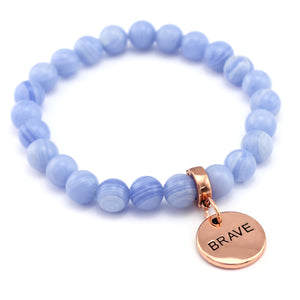 Blue beaded bracelet with a rose gold 'BRAVE' charm on a white background