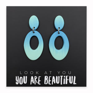 Blue earrings on a black card with motivational text