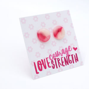 A pair of round pink and white marbled stud earrings displayed on a white backing card with a light pink floral pattern and the words 'courage LOVE STRENGTH' in pink lettering.