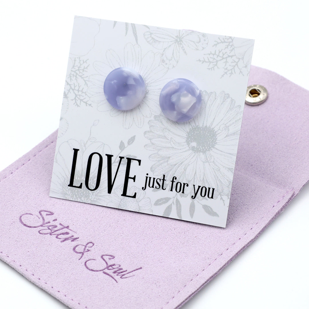 A pair of round lavender and white marbled stud earrings displayed on a white floral card that reads 'LOVE just for you', resting on a light purple pouch embroidered with 'Sister & Soul'.
