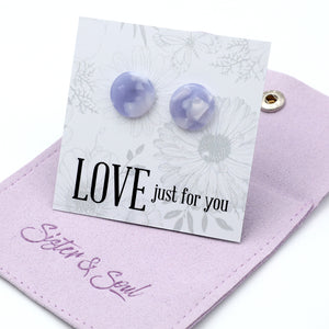 A pair of round lavender and white marbled stud earrings displayed on a white floral card that reads 'LOVE just for you', resting on a light purple pouch embroidered with 'Sister & Soul'.