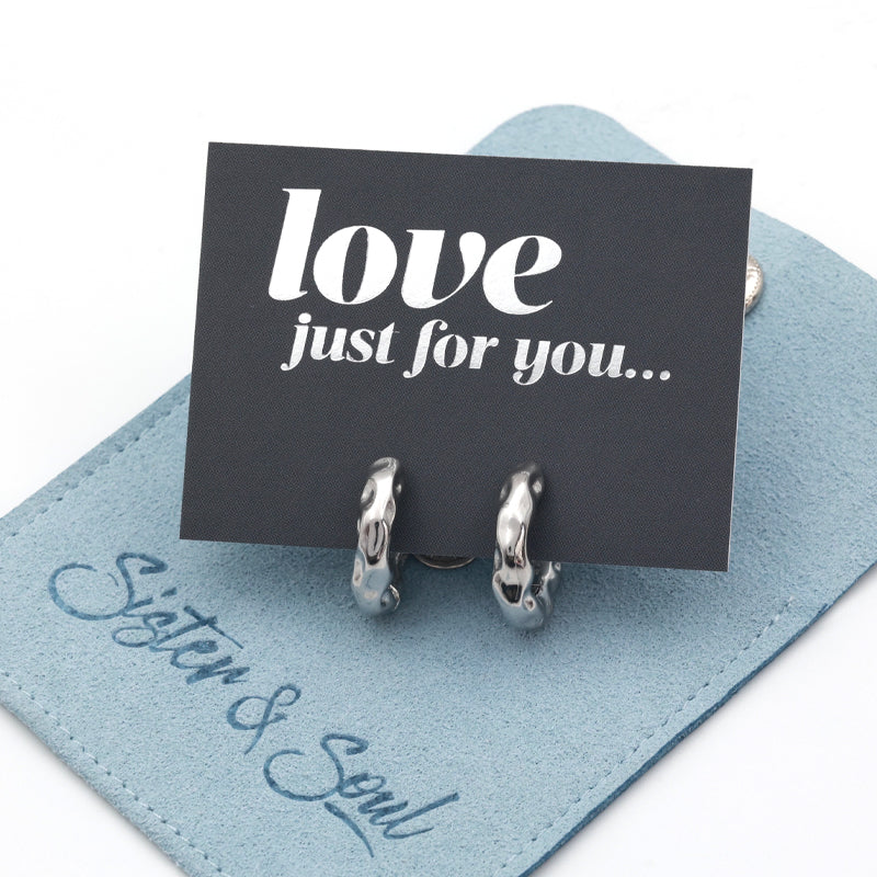 Silver Huggies hoop earrings on a grey card with silver wording that says "love just for you" on top of a blue pouch on a white background