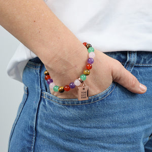 Colorful beaded bracelet with a tag on a wrist, worn with blue jeans and a white shirt.