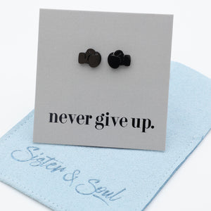 A pair of small black boxing gloves stud earrings displayed on a light gray card that reads 'never give up.' with a light blue fabric pouch underneath.