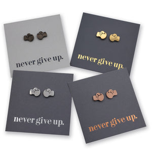 Four pairs of small boxing glove stud earrings displayed on dark gray backing cards with the phrase "never give up." printed on them.