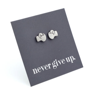 A pair of small silver stud earrings shaped like boxing gloves, displayed on a dark gray backing card that reads 'never give up.' on a white background.
