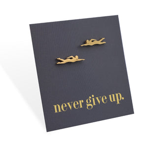 Gold swimming earrings on a black card with 'never give up.' text