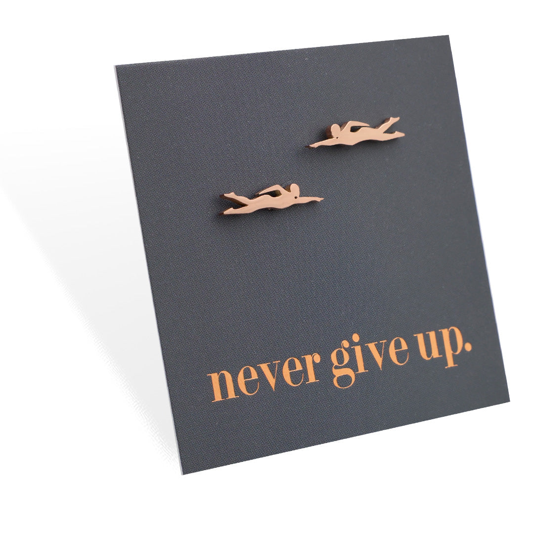 Two small swimming figurine earrings on a dark card with 'never give up' text