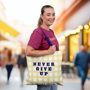 Woman holding a yellow tote bag with 'Never Give Up' text in a blurred indoor setting