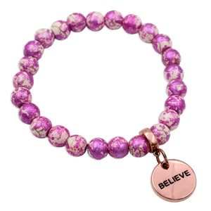 Pink beaded bracelet with a 'BELIEVE' charm on a white background