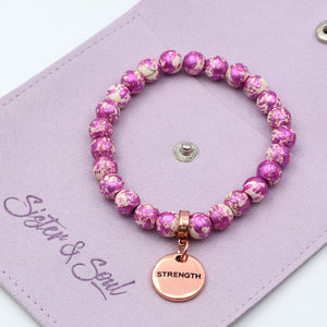 Pink beaded bracelet with 'Strength' charm on a purple card with 'Sister & Soul' branding.
