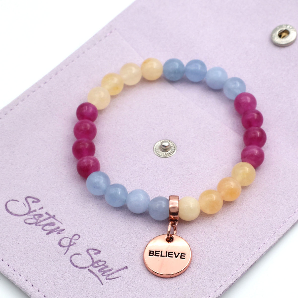 Multicolored beaded bracelet with 'BELIEVE' charm on a pink card with 'Sister & Soul' branding.