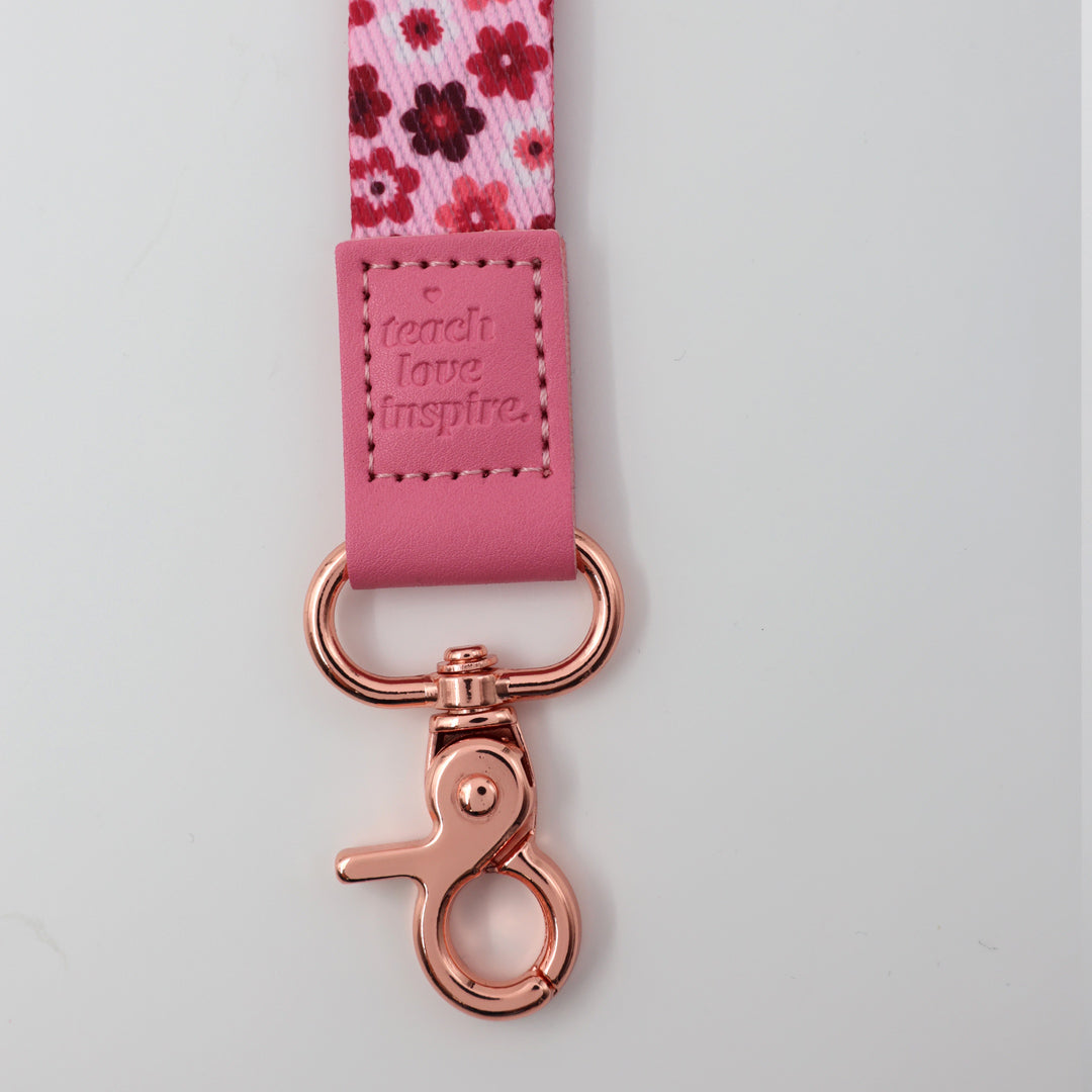 Pink lanyard with floral pattern and rose gold clasp on a light gray background