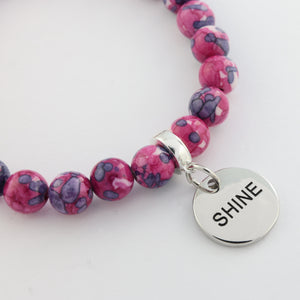 Pink beaded bracelet with a silver 'SHINE' charm on a white background