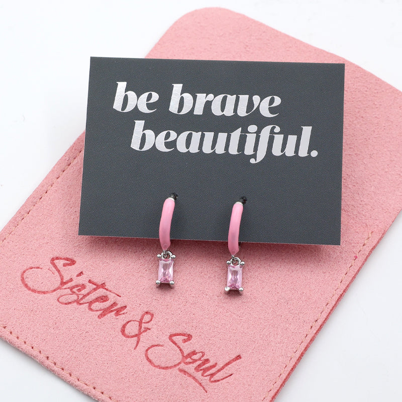 Pink earrings on a 'be brave beautiful' card with a pink background