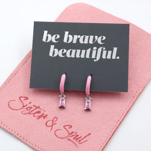 Pink earrings on a 'be brave beautiful' card with a pink background