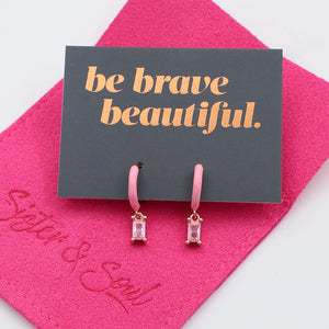 Pink earrings on a 'be brave beautiful' card with a pink background