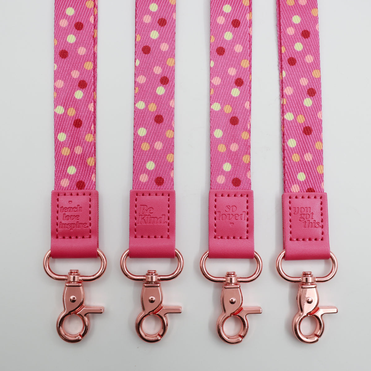 Pink Polka lanyards showing Be Kind, Teach Love Inspire, You Got This and So Loved embossed trims and lobster clasps.
