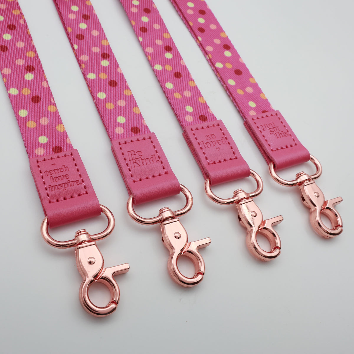 Pink Polka lanyards showing Be Kind, Teach Love Inspire, You Got This and So Loved embossed trims and lobster clasps.