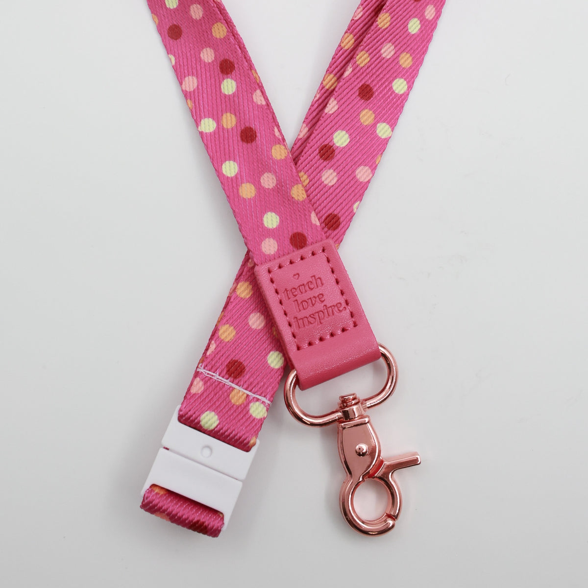 Teach Love Inspire embossed on a pink polka dot lanyard with pink trim and a lobster clasp.