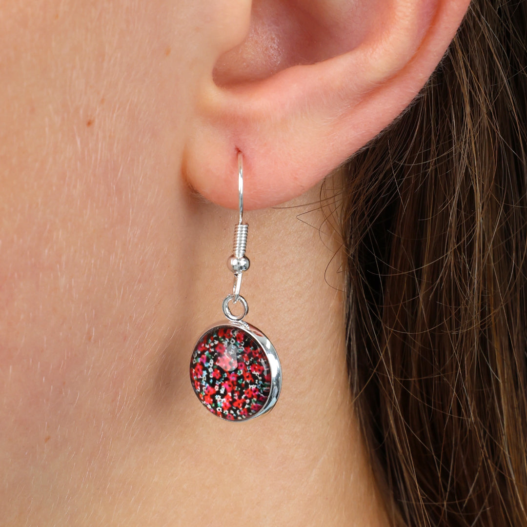 Close-up of a person wearing a silver earring with a red and black speckled design.