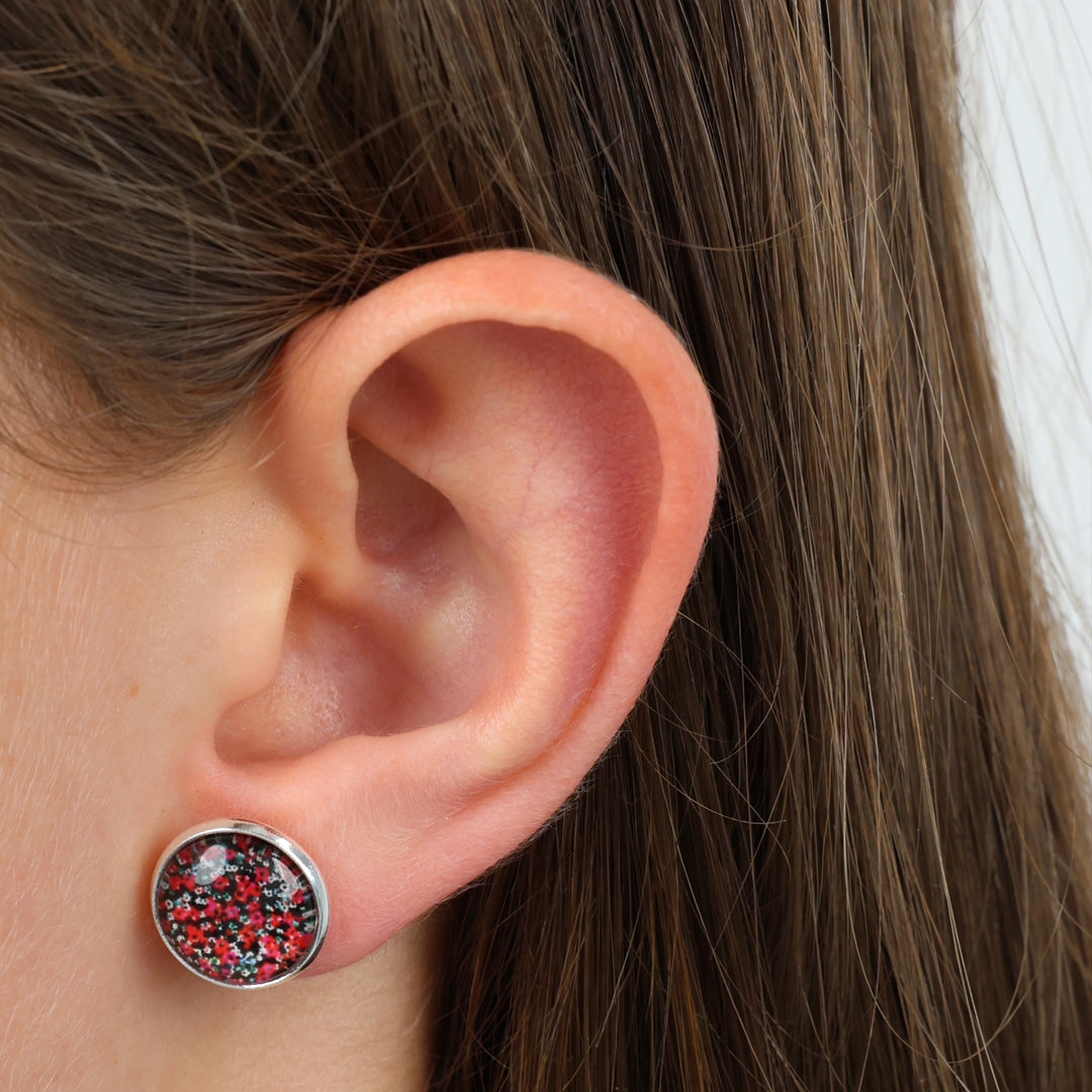 Close-up of an ear wearing a round earring with a silver border and multicolored stones.
