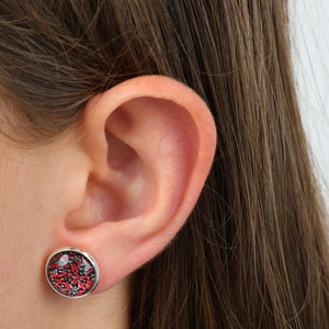 Close-up of an ear wearing a round earring with a silver border and multicolored stones.