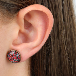 Close-up of an ear wearing a colorful stud earring with a blurred background