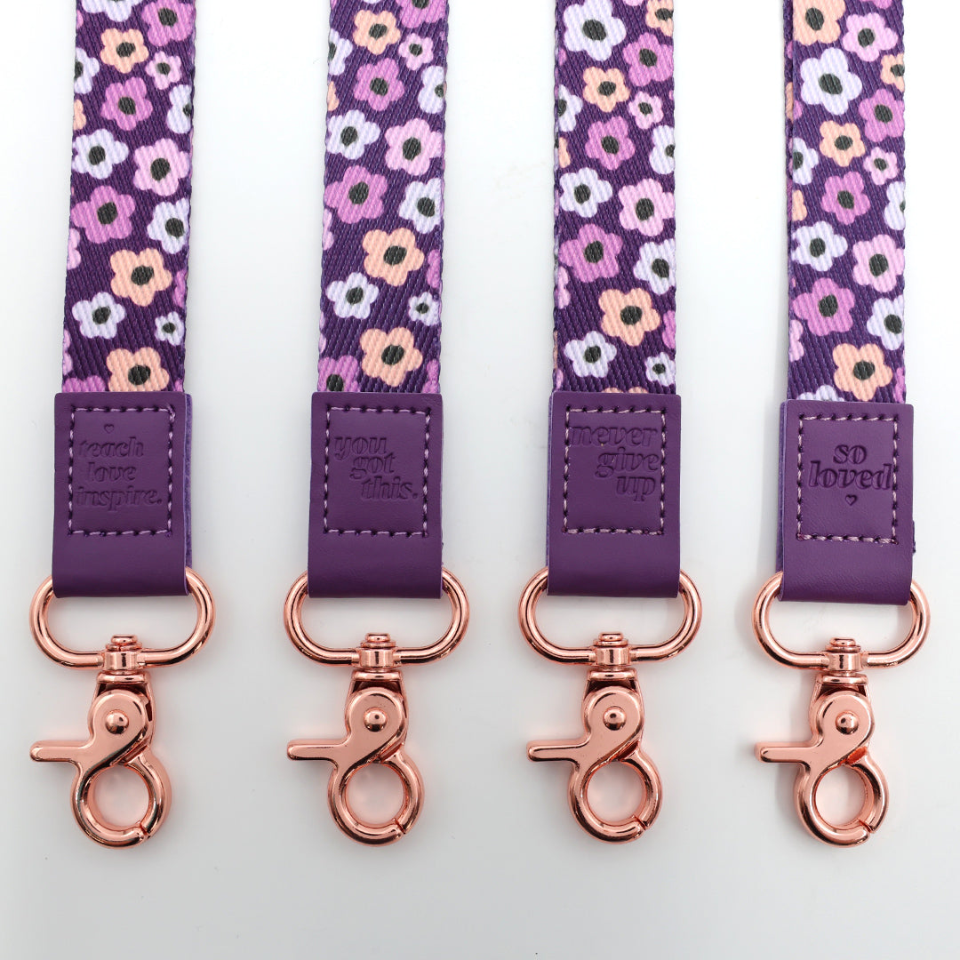 Four floral-patterned lanyards with purple straps and rose gold hooks on a white background.