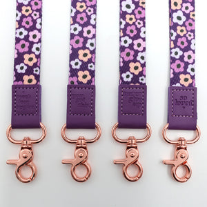 Four floral-patterned lanyards with purple straps and rose gold hooks on a white background.