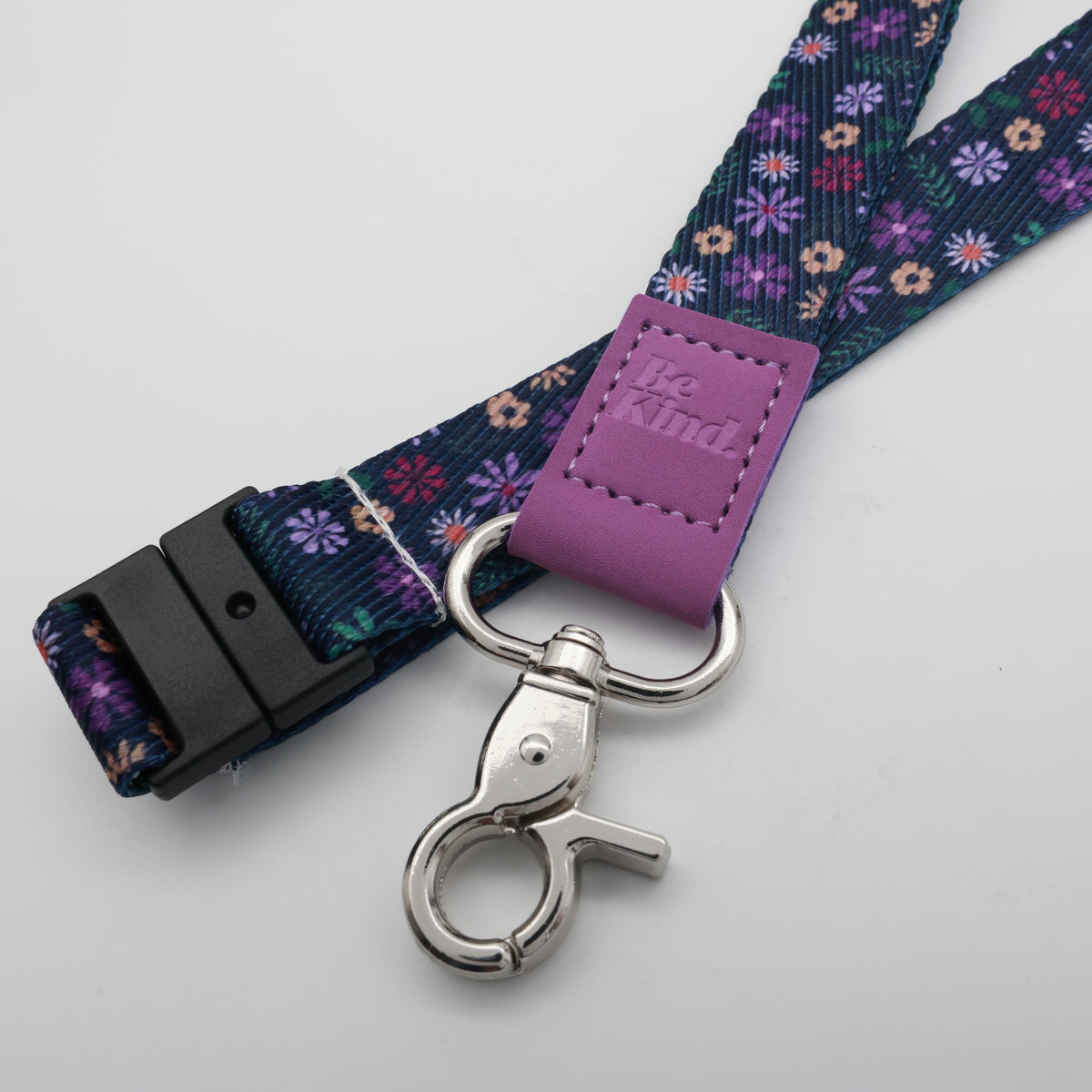 Be Kind embossed on a navy floral lanyard with purple trim and a lobster clasp.