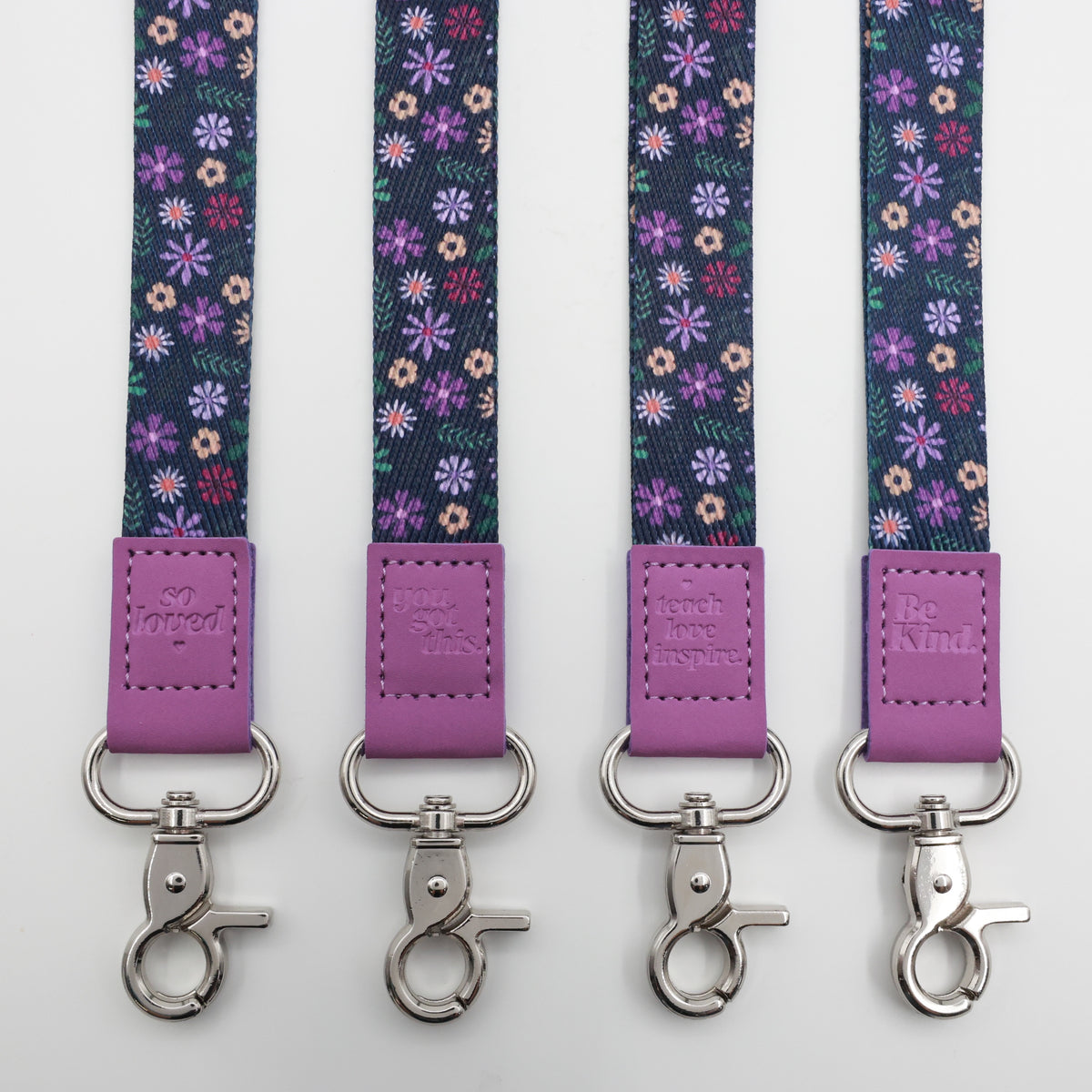 Purple Floral lanyards showing Be Kind, Teach Love Inspire, You Got This and So Loved embossed trims and lobster clasps.