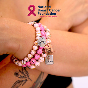 Bracelet with motivational charms on a wrist, featuring the National Breast Cancer Foundation logo.