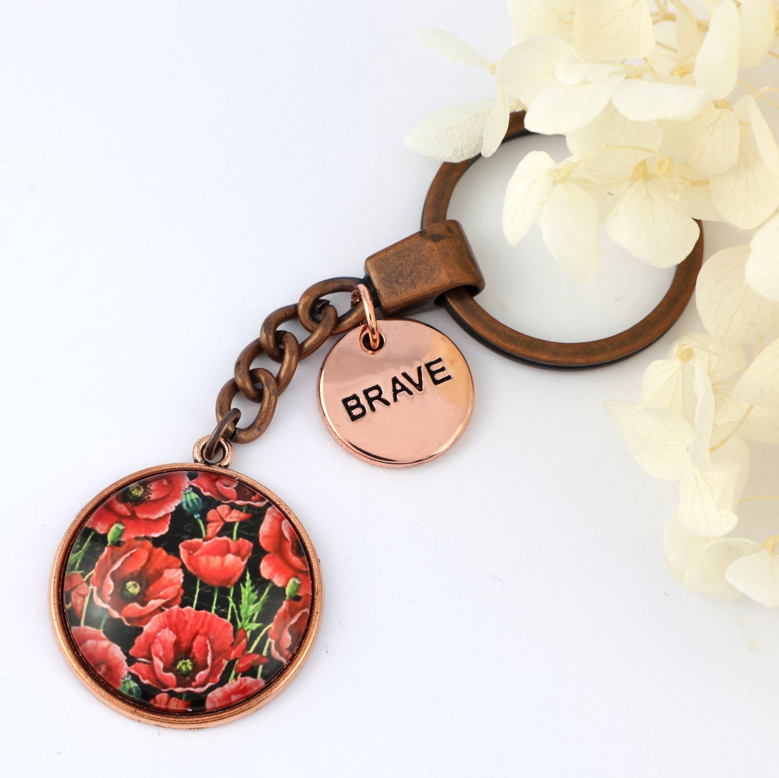 Keychain with floral design and 'BRAVE' tag on a white background