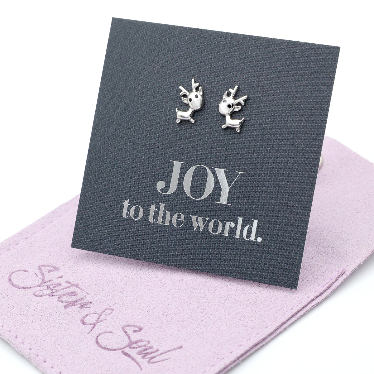 Silver reindeer earrings on a card with 'JOY to the world.' text, placed on a pink fabric surface with 'Sister & Soul' branding.