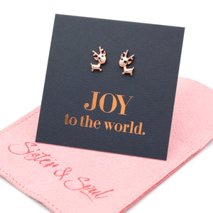 Rose gold reindeer earrings on a card with 'JOY to the world' text, placed on a pink cloth with 'Sister & Swirl' branding.