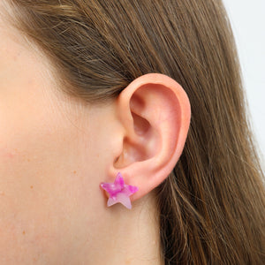 Close-up of an ear wearing a pink star-shaped earring with a neutral background