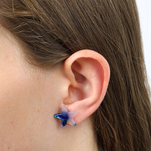 Star-shaped blue and clear earring worn by a person with brown hair.