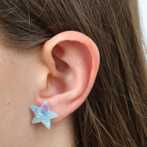 Star-shaped earring worn on a person's ear with brown hair.