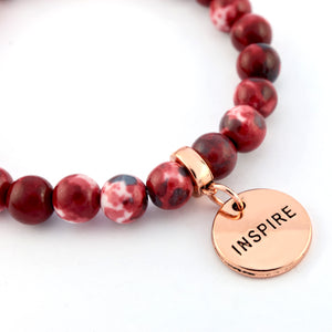 Bracelet with red beads and a rose gold charm with 'INSPIRE' on a white background