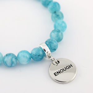 Turquoise beaded bracelet with a silver 'ENOUGH' charm on a white background