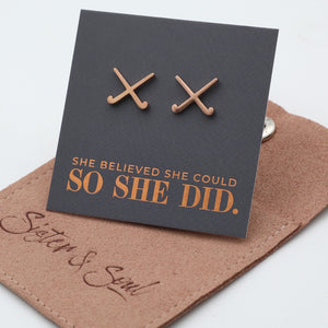 Rose gold hockey shaped earrings on a card with 'She believed she could so she did' text, on a brown surface with 'Sister & Soul' branding.