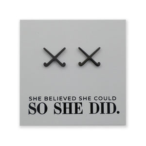 Black field hockey earrings on a grey card with 'She believed she could so she did' text